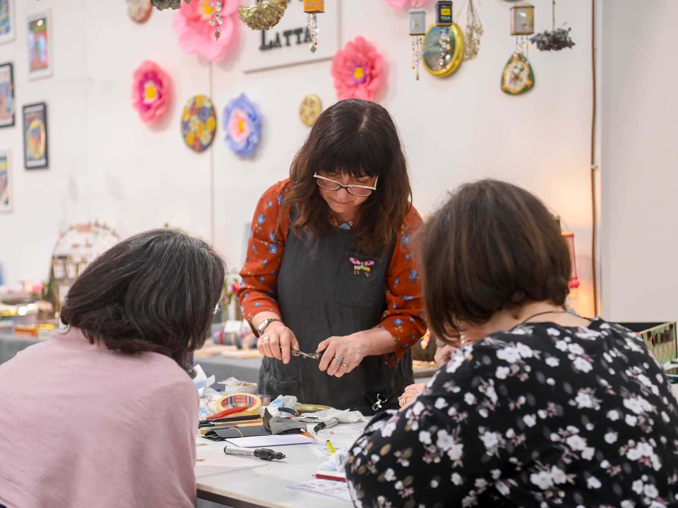 Person guiding two participants in a hands-on creative workshop at Abilmente among materials and colorful decoration