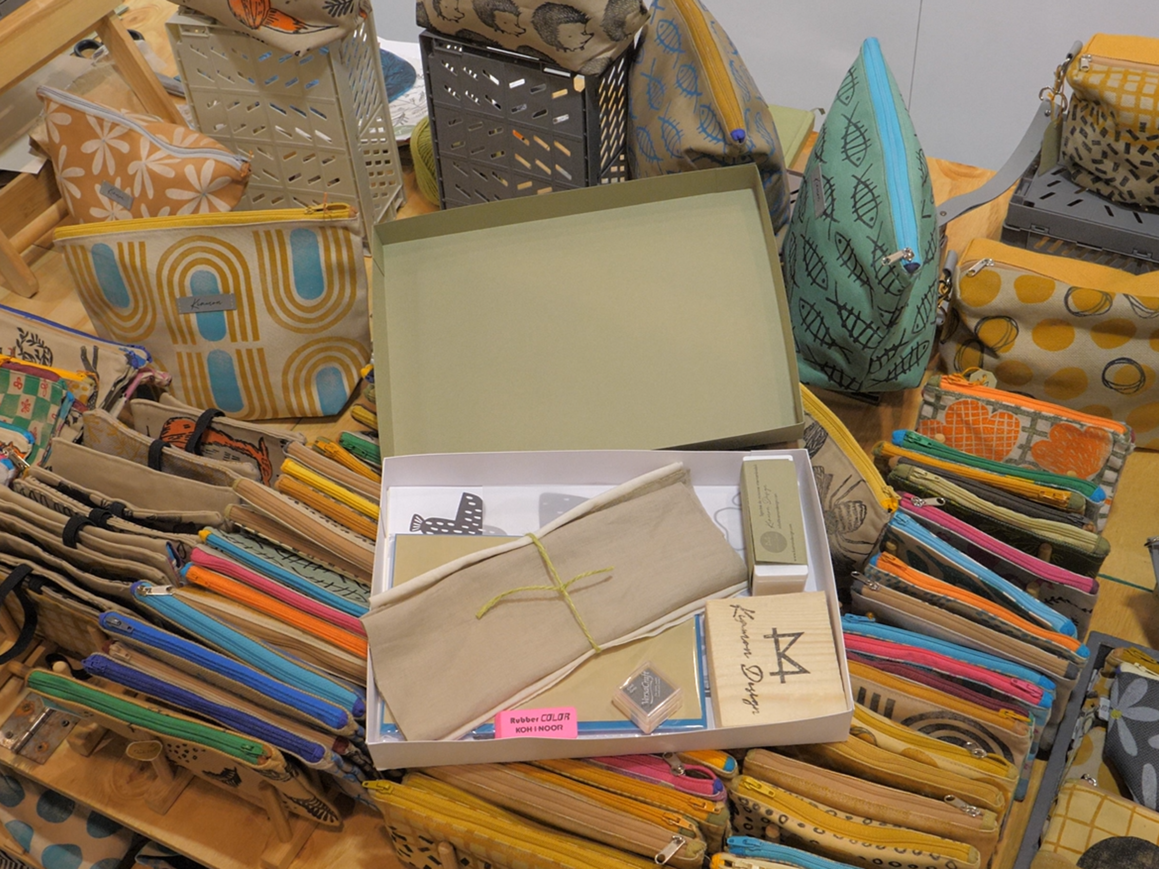 A display featuring bags, pouches, and clutches made of fabric in bright colors and geometric patterns, on display at the Abilmente craft fair.